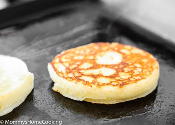 two egg-free lemon ricotta pancakes being cooked in a skillet. 