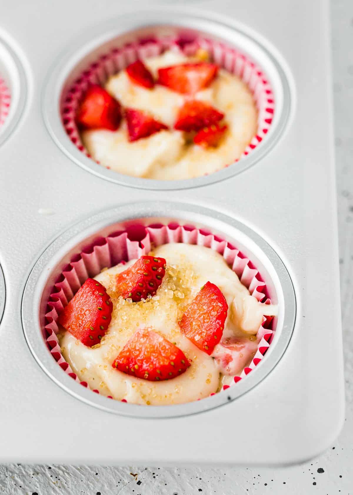 unbaked egg-free strawberry muffins in a muffin pan with turbinado sugar on top. 