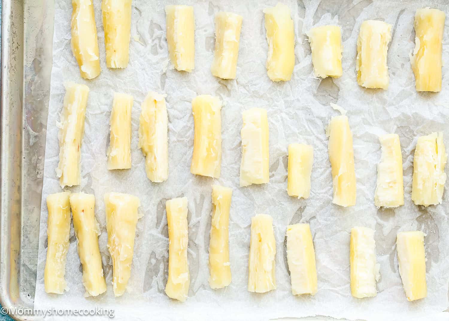 Several pieces of peeled and cut yuca (cassava) are arranged on a parchment-lined baking sheet, showing the first step in How to Make Yuca Fries, ready for cooking.