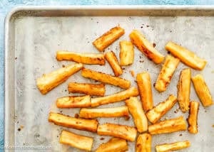 Baked yuca fries are scattered on a metal baking sheet with a lightly browned surface, perfectly crisped for anyone wanting to learn how to make yuca fries at home.