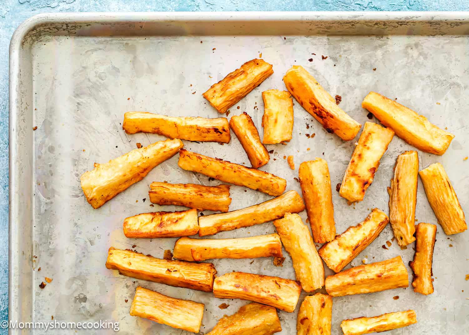 Baked yuca fries are scattered on a metal baking sheet with a lightly browned surface, perfectly crisped for anyone wanting to learn how to make yuca fries at home.
