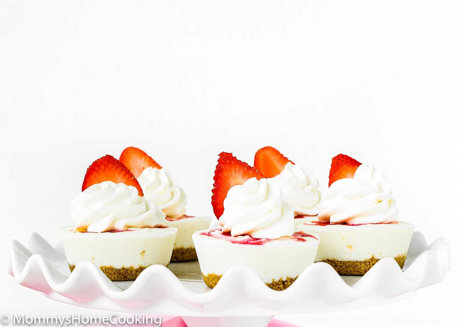 Mini Greek Yogurt Strawberry Cheesecakes in a serving plate topped with fresh strawberries.
