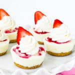 Mini Yogurt Strawberry Cheesecake with whipped cream and a fresh strawberry on a cake stand.