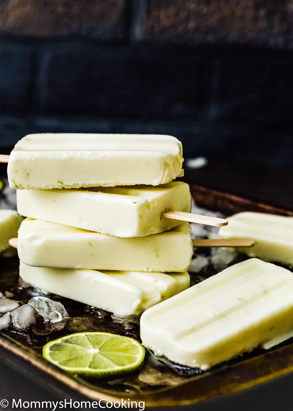 stack of key lime popsicles on a tray with ice and lime slices.