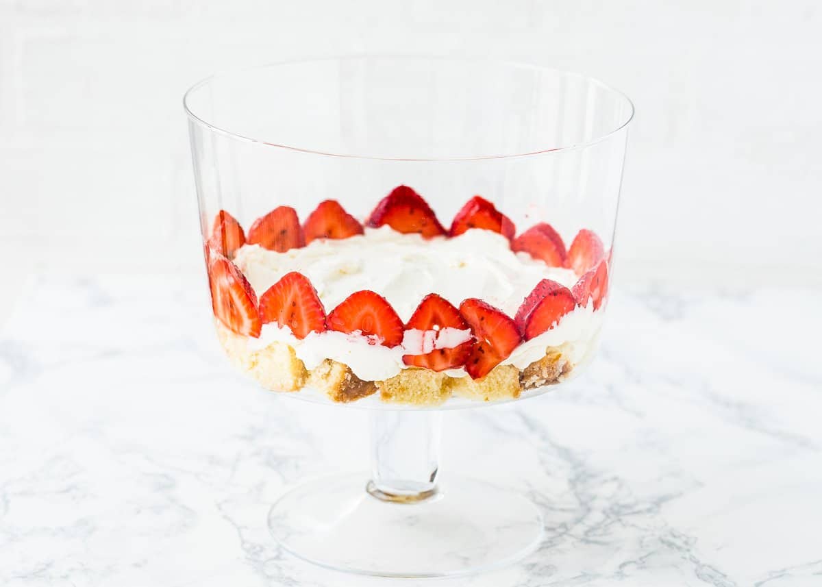 cubed egg-free pound cake on the bottom of a trifle dish topped with whipped cream and strawberries. 