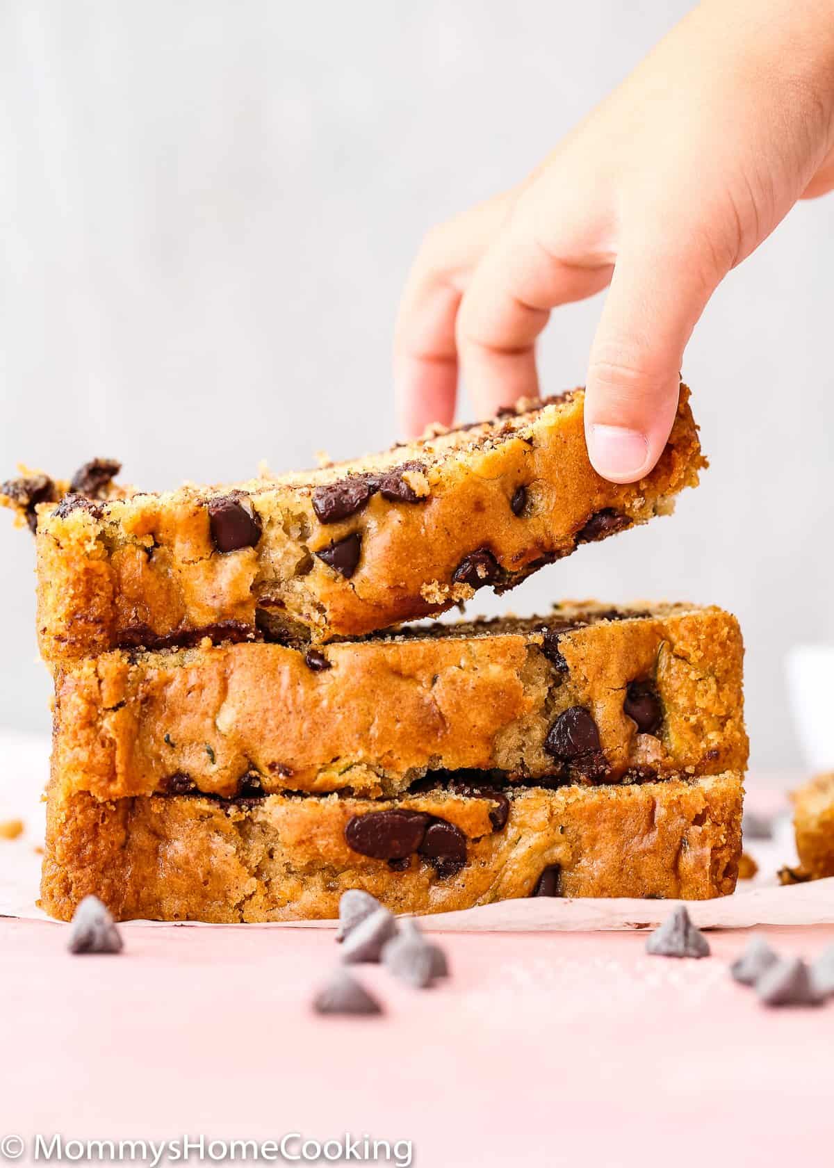 a hand pick a slice of eggless zucchini bread with chocolate chips