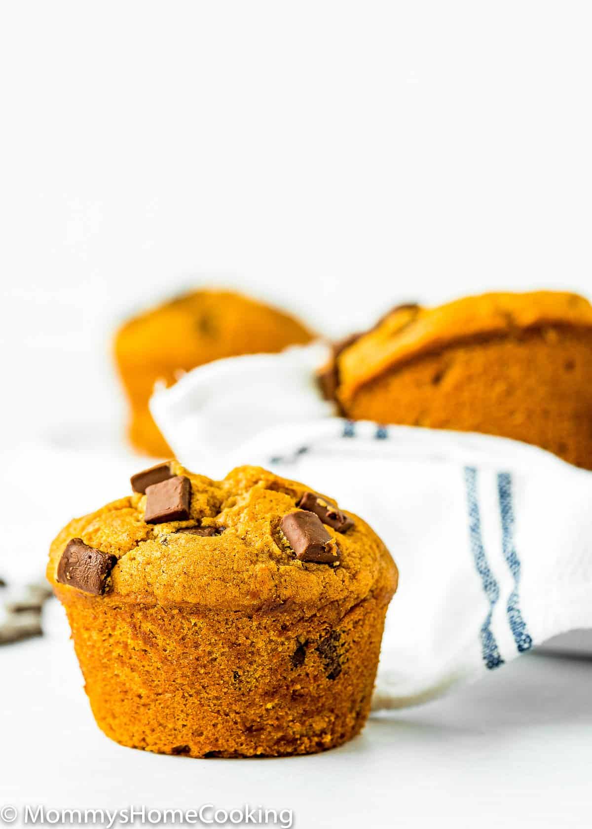 Eggless Chocolate Chip Pumpkin Muffin on a white surface with more muffins on the background