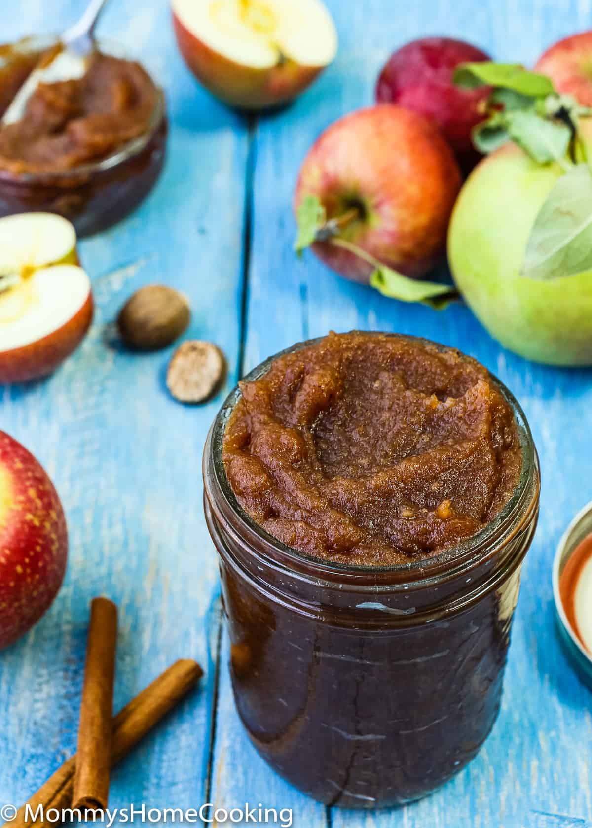 apple butter in a mason jar with fresh apples and cinnamon on the sides