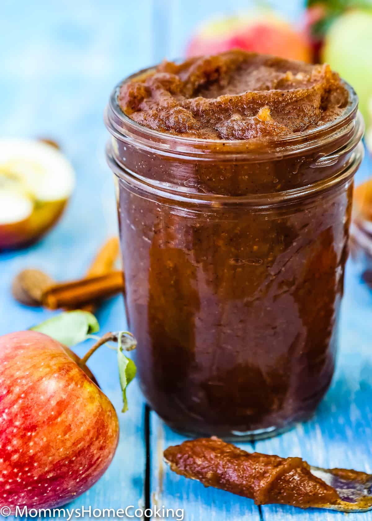 apple butter in a glass jar with a butter knife on the side