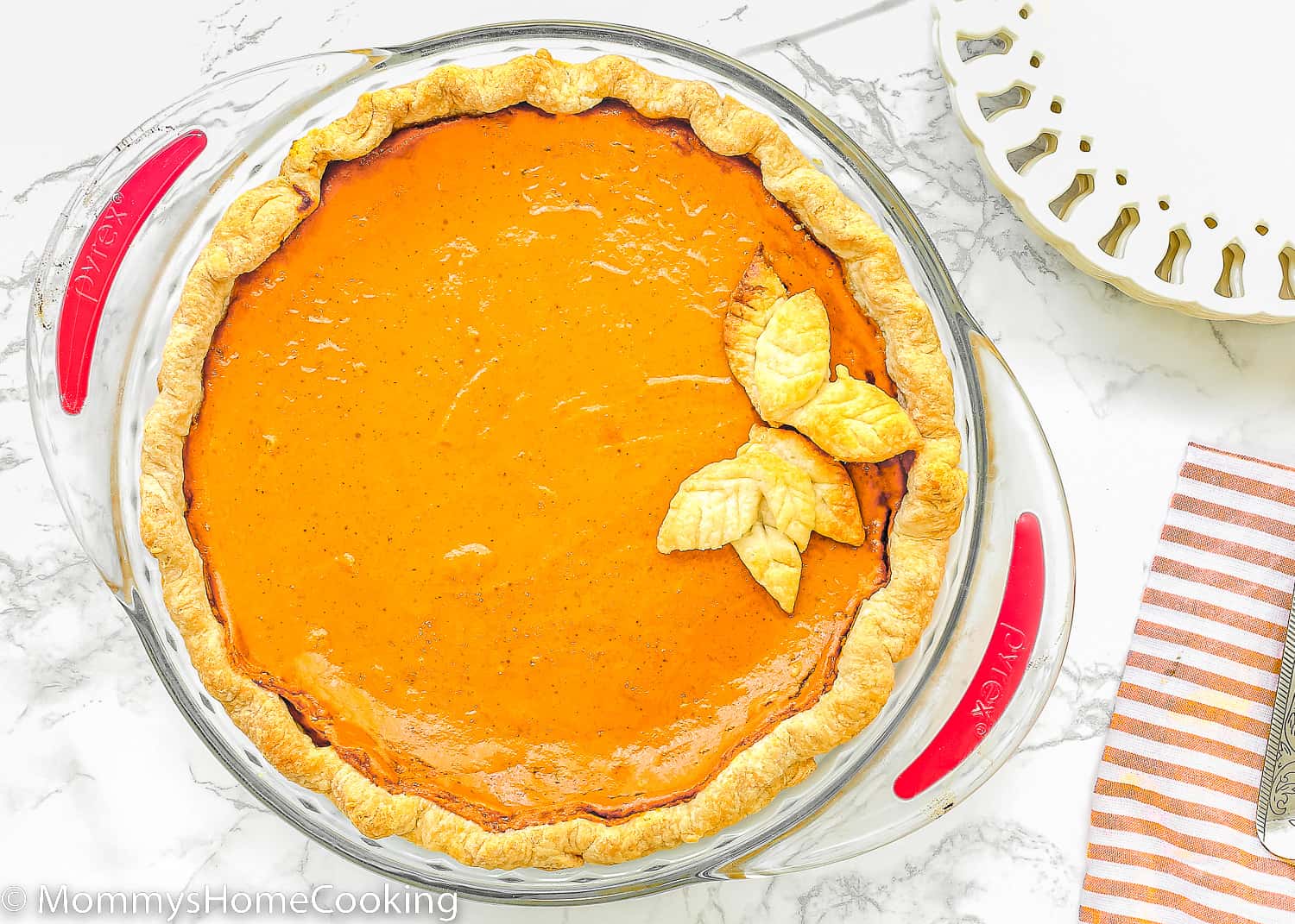 baked egg-free pumpkin pie in a pie dish with a kitchen towel and white desserts plates on the side. 