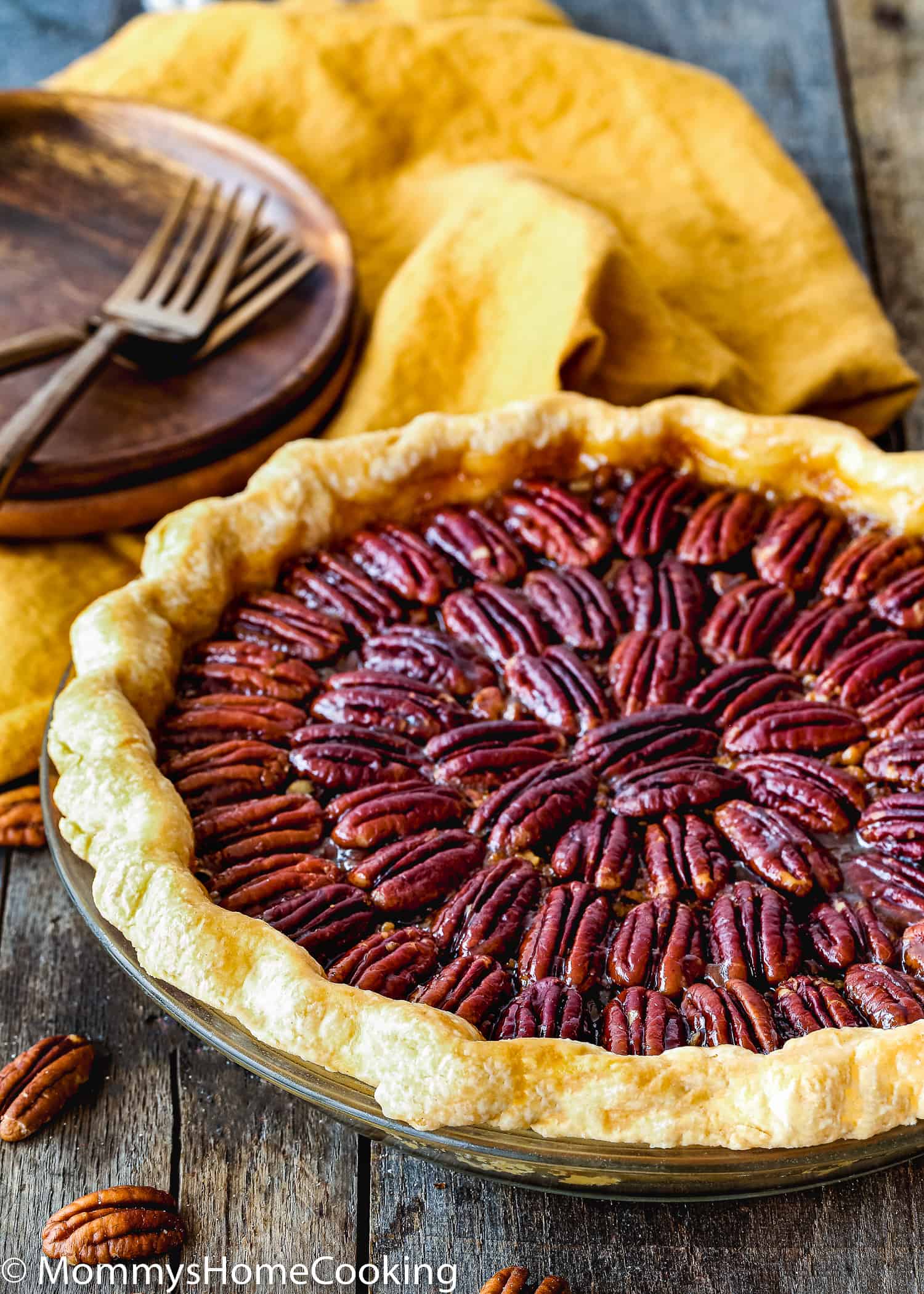 egg-free pecan pie in a pie dish over a wooden surface with a yellow kitchen towel, wooden plates and forks in the background.