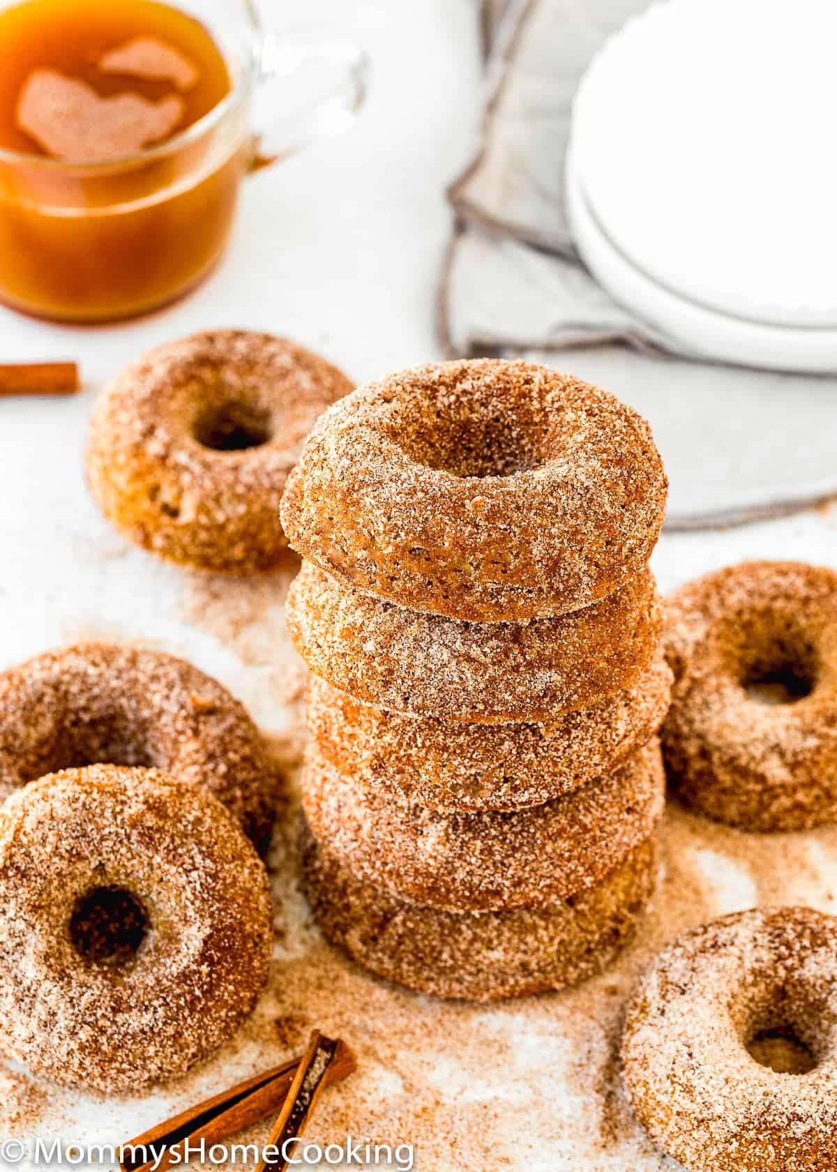 Eggless Apple Cider Donuts with sugar and cinnamon over a white surface and glass of apple cider in the background 