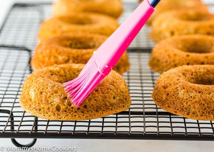 a kitchen brush brushing Eggless Apple Cider Donuts with butter