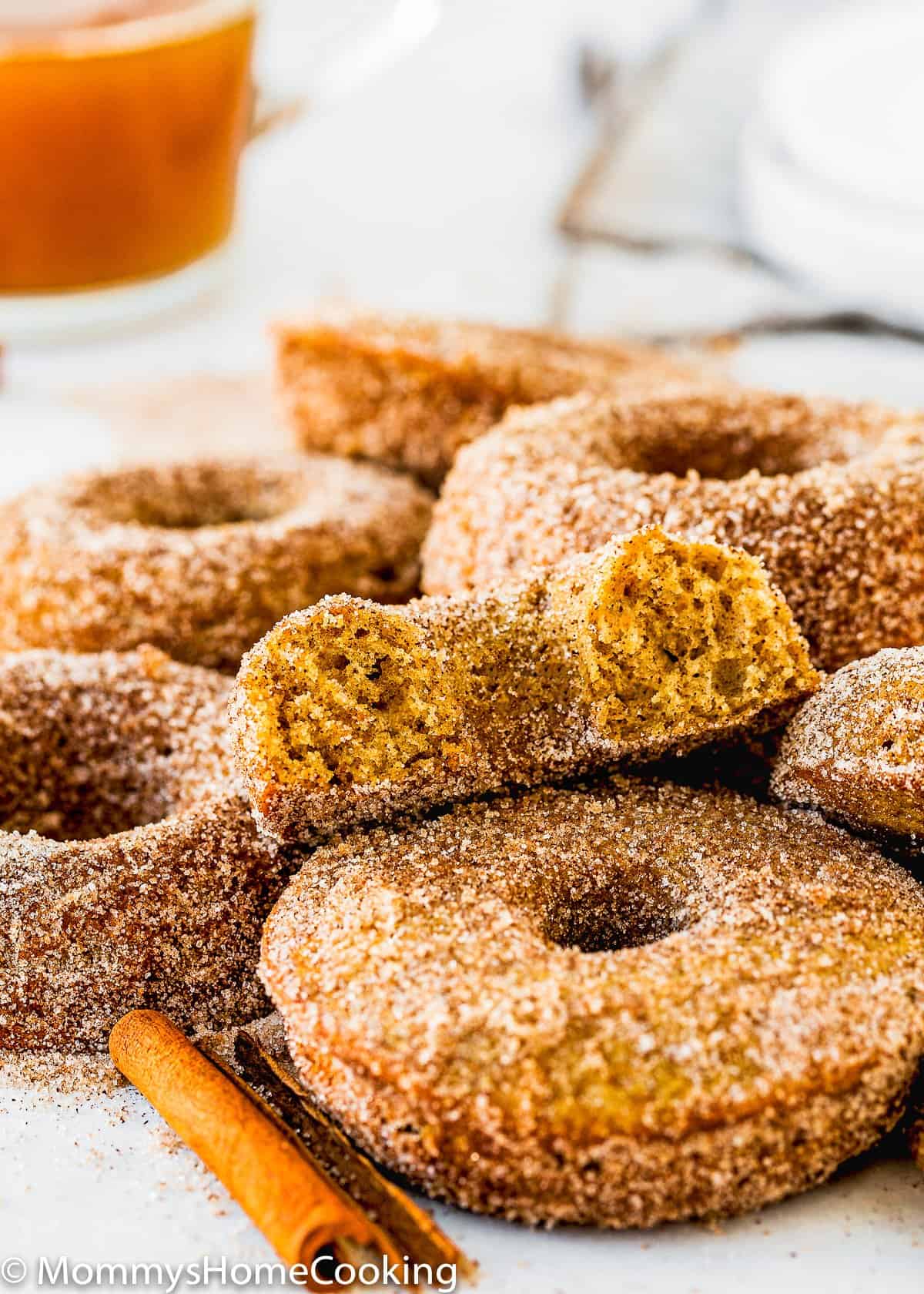 bitten Eggless Apple Cider Donut showing its fluffy inside texture with a glass of apple cider in the background