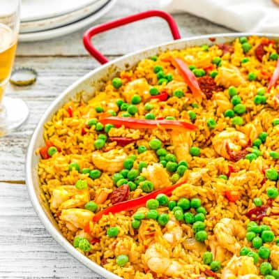 Spanish Paella in a paella pan with plate and a cup of beer in the background