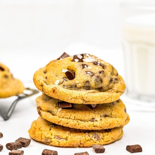 A stack of THE BEST Eggless Chocolate Chip Cookies sits next to a glass of milk.