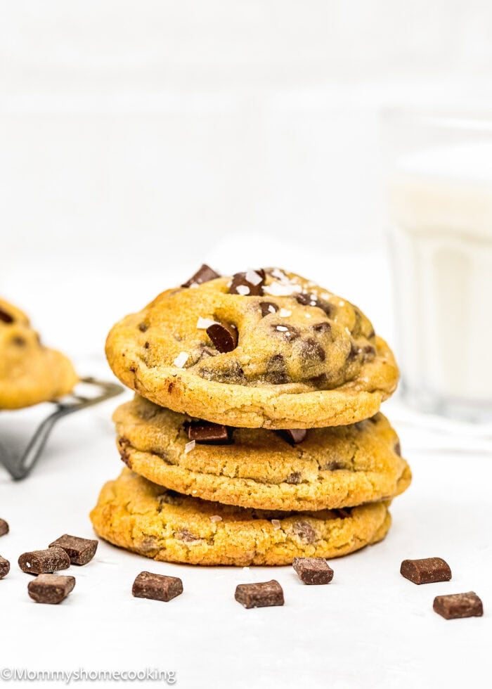 A stack of THE BEST Eggless Chocolate Chip Cookies sits next to a glass of milk.