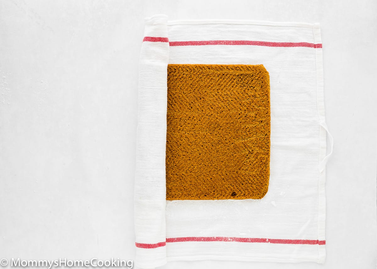 Eggless Pumpkin Roll being rolled in a kitchen towel