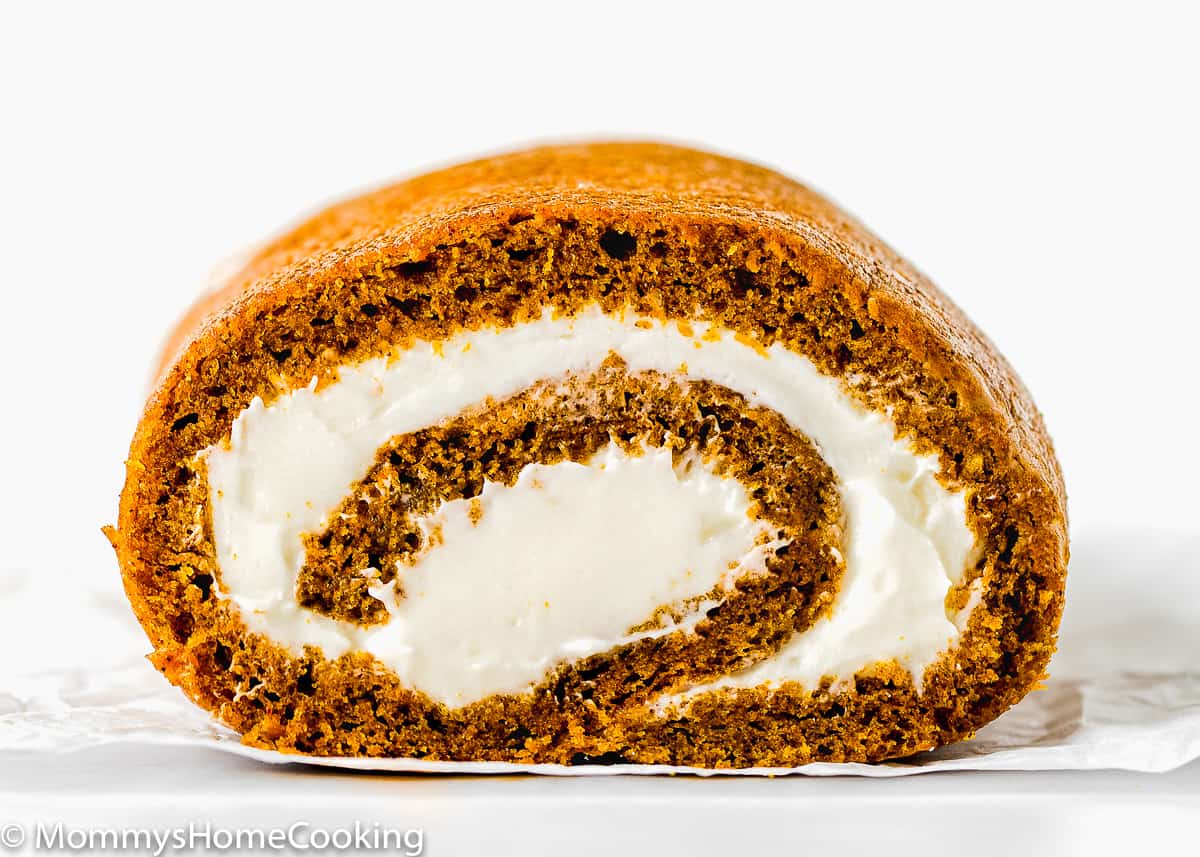 Eggless Pumpkin Roll filled with cream cheese frosting over a parchment paper