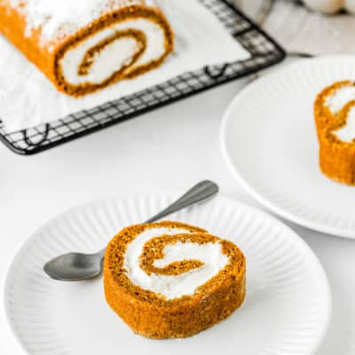 Eggless Pumpkin Roll slice with the whole pumpkin roll in the background