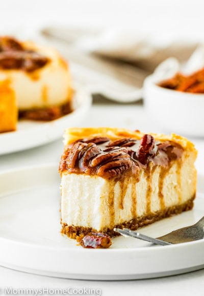 egg-free pecan pie cheesecake slice on a white plate with a fork on the side.