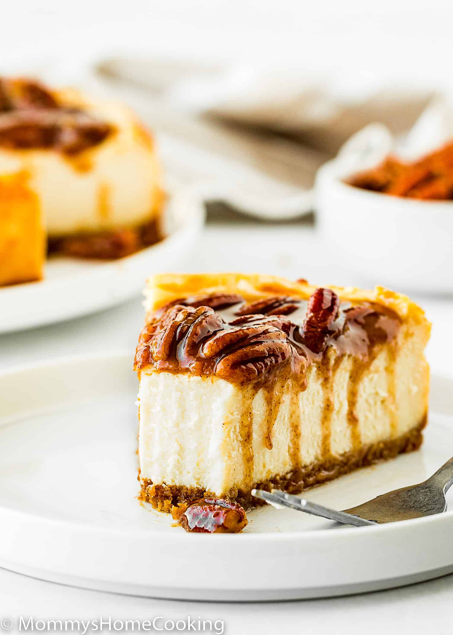 egg-free pecan pie cheesecake slice on a white plate with a fork on the side.