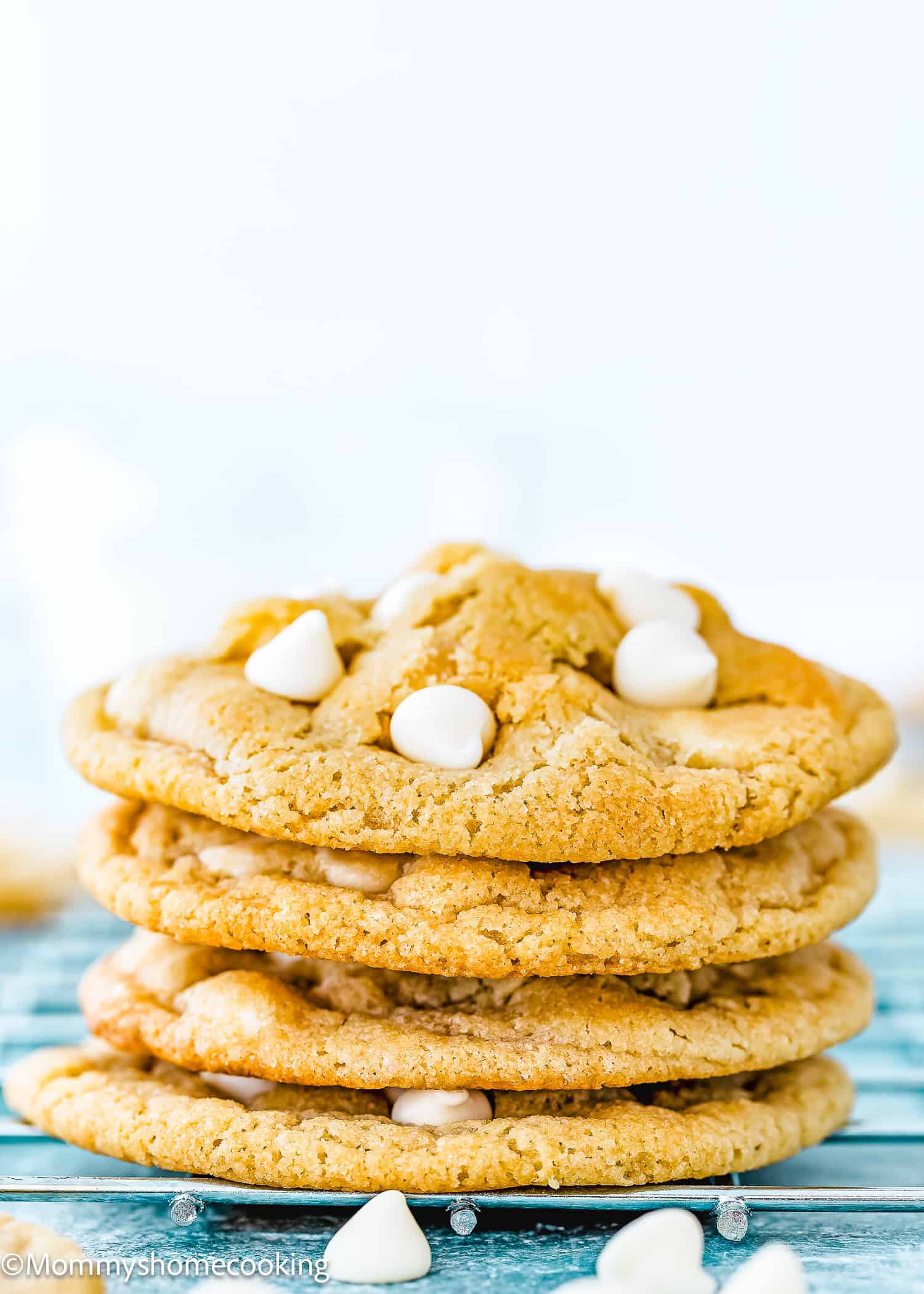 A stack of four eggless white chocolate cookies sits invitingly on a blue wooden surface.