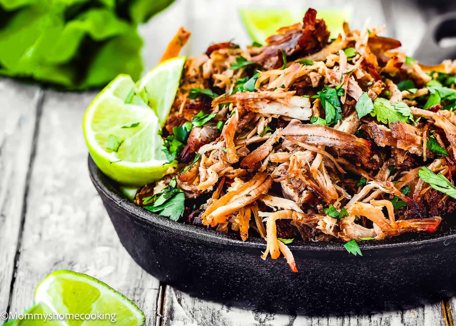 Shredded, seasoned Instant Pot Crispy Pork Carnitas garnished with lime wedges and cilantro on a dark plate.