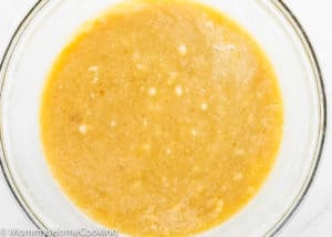 A clear glass bowl filled with a light brown, slightly lumpy batter mixture, perfect for making the BEST Eggless Banana Bread.