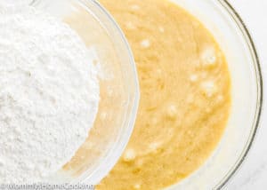 A glass bowl of flour sits beside a glass bowl containing yellow batter for the BEST Eggless Banana Bread, viewed from above.