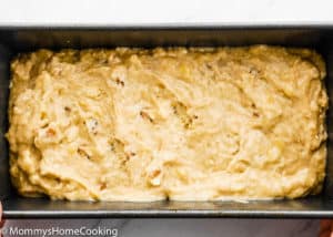 A metal loaf pan filled with unbaked BEST Eggless Banana Bread batter sits on a white surface.