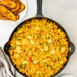 easy arroz con pollo in a skillet with plantains on the side.
