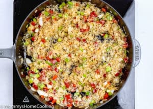 un cooked rice and veggies being sautéed in a skillet.