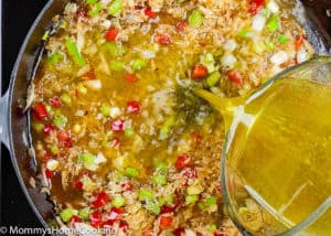 chicken broth being poured to a skillet with rice and veggies.