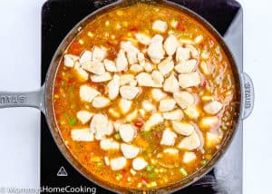 pieces of chicken breast being added to rice in a skillet.