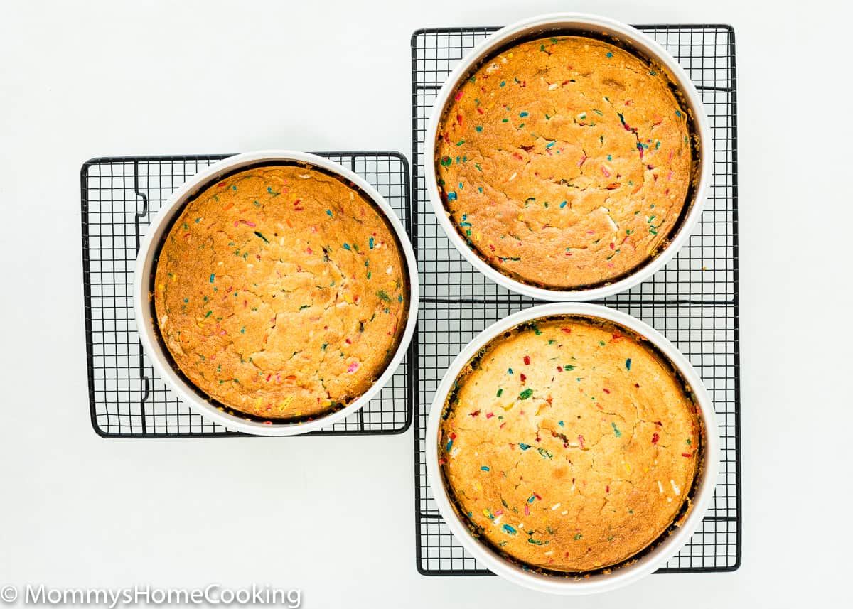 three egg-free cakes in cake pans over cooling racks.