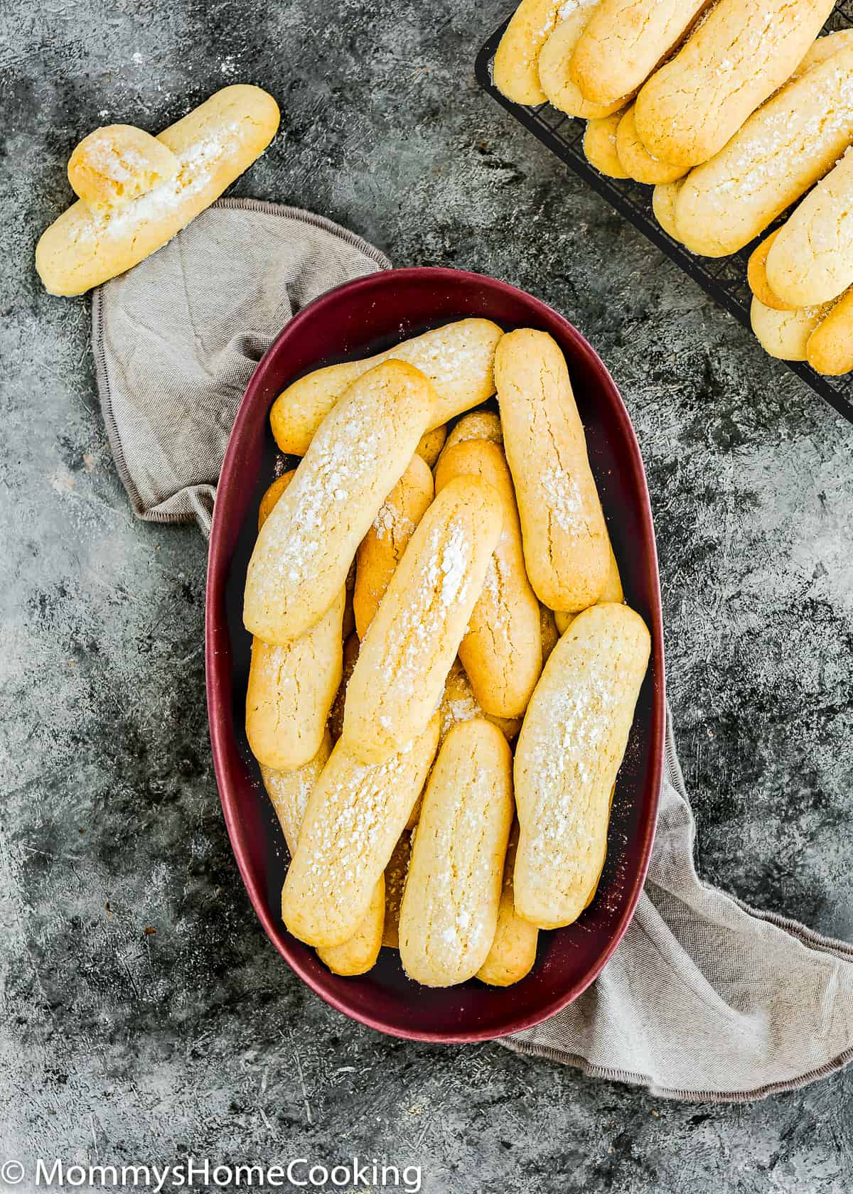 eggless ladyfinger cookies over a in a bowl and over a cooling rack.
