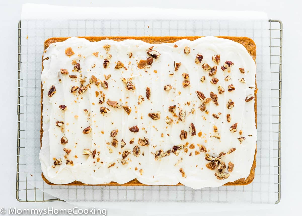 whole egg-free pineapple carrot cake with cream cheese frosting and chopped pecans over a cooling rack.