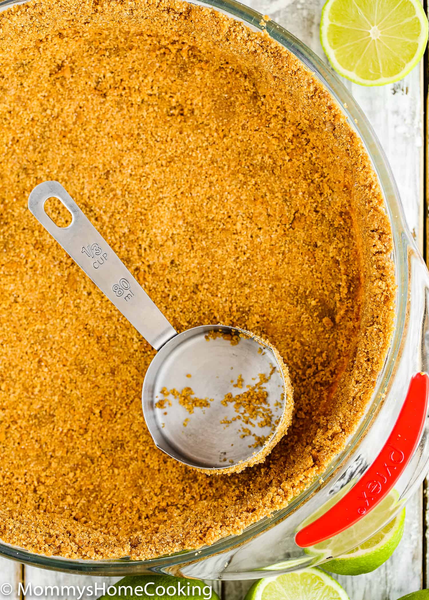 a measuring cup pressing down graham cracker crust in a pie dish.