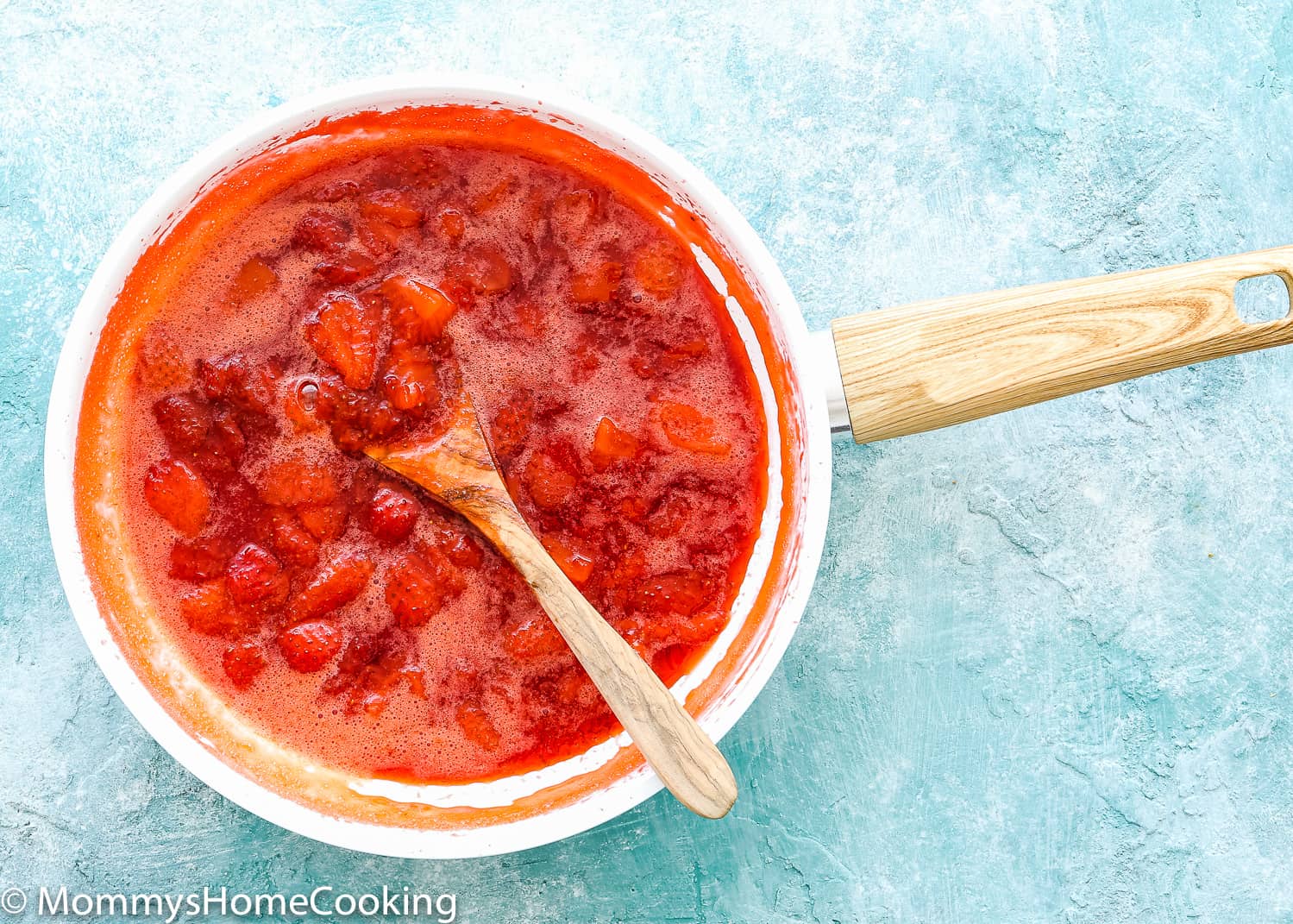 strawberry sauce topping in a skillet with a wooden spoon.
