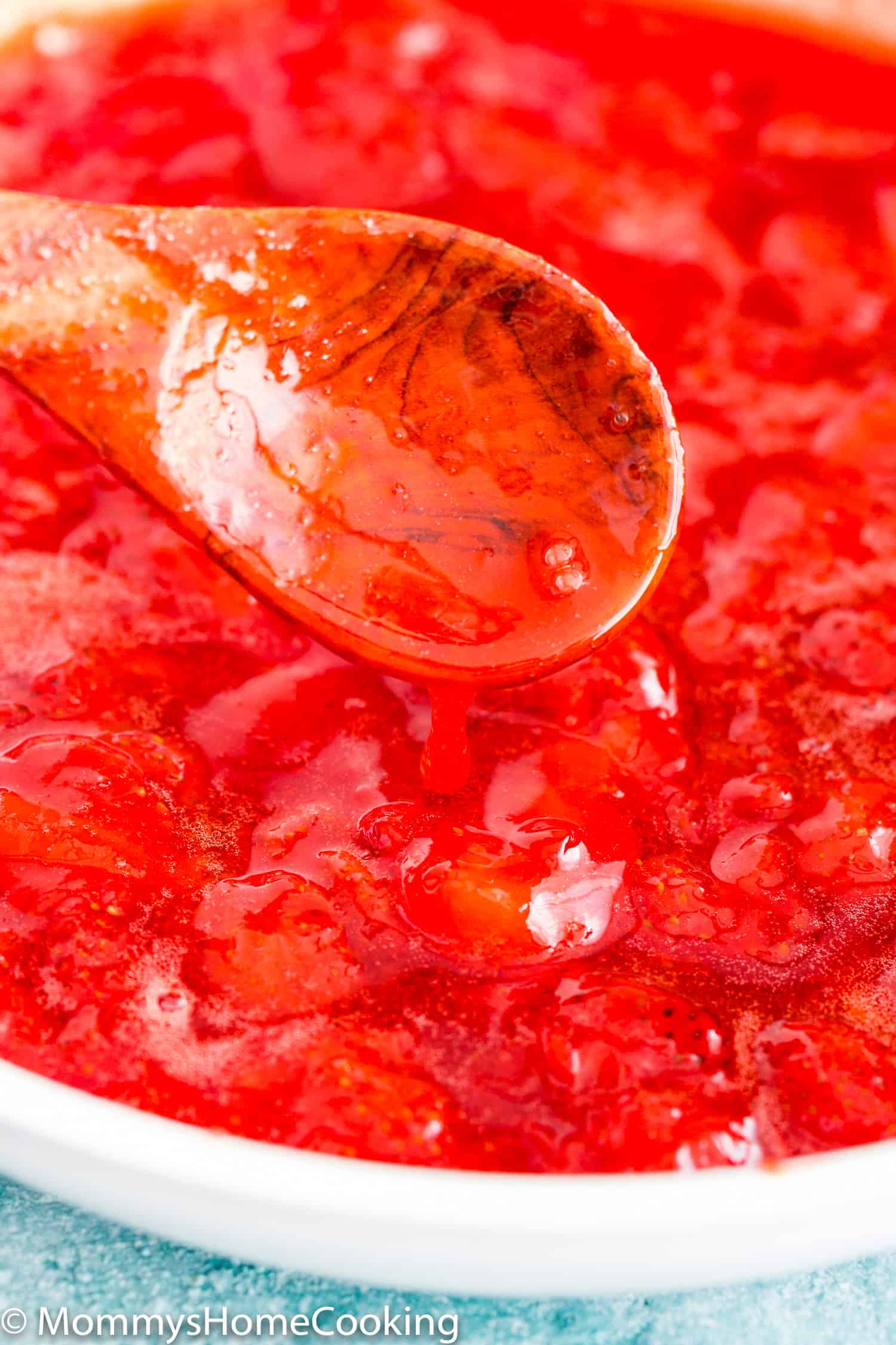 a wooden spoon with thicken strawberry sauce topping.