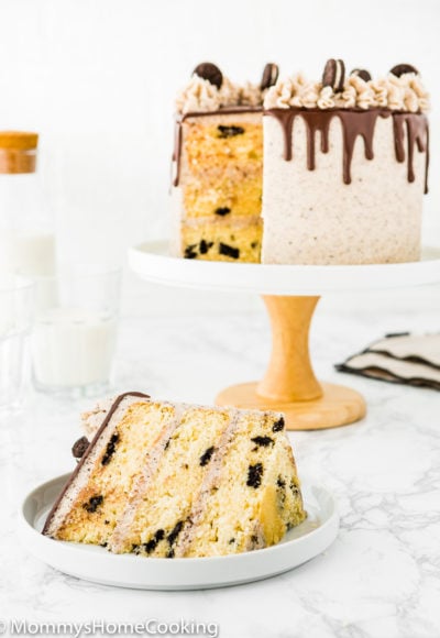 a slice of egg-free oreo cake on a white plate with the whole cake on the background.