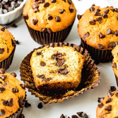 one Eggless Banana Chocolate Chip Muffin cut open with other muffins around it.