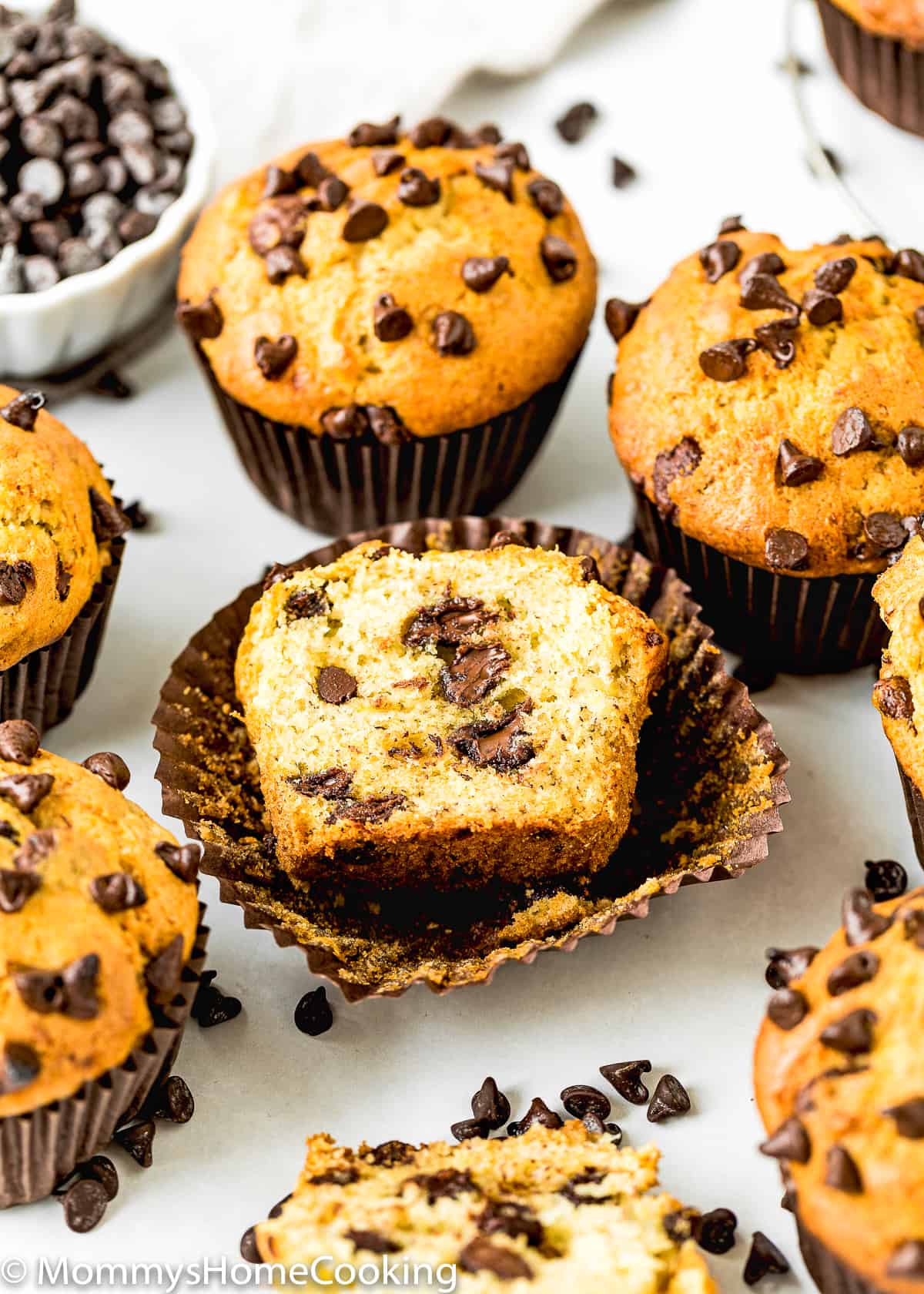 one Eggless Banana Chocolate Chip Muffin cut open with other muffins around it.