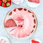 a egg-free Strawberry Bundt Cake on a plate over a blue surface with fresh strawberries around.