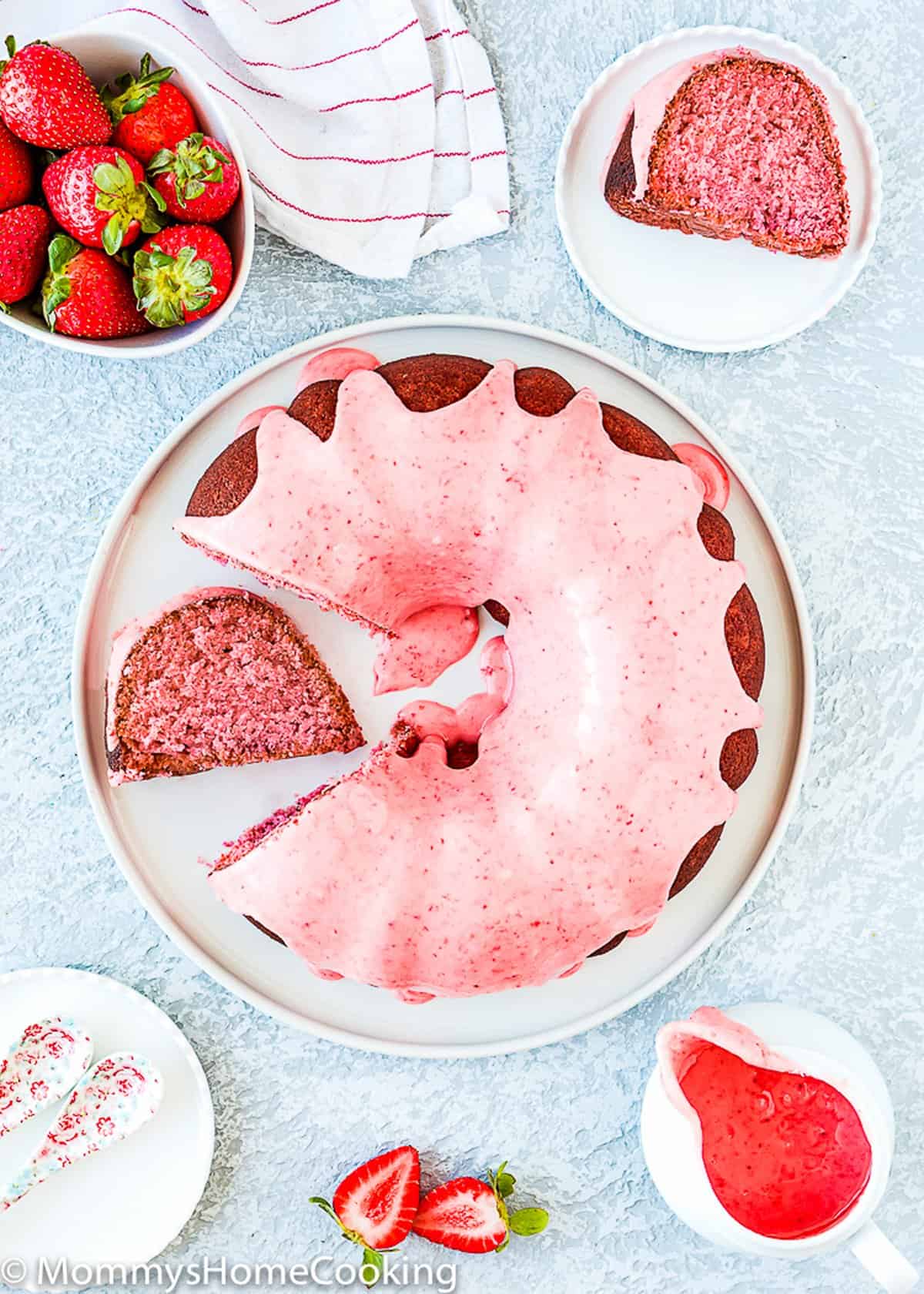 a egg-free Strawberry Bundt Cake on a plate over a blue surface with fresh strawberries around.