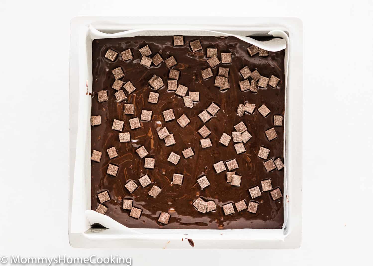 eggless brownie batter with chocolate chunks on top in a square baking pan.