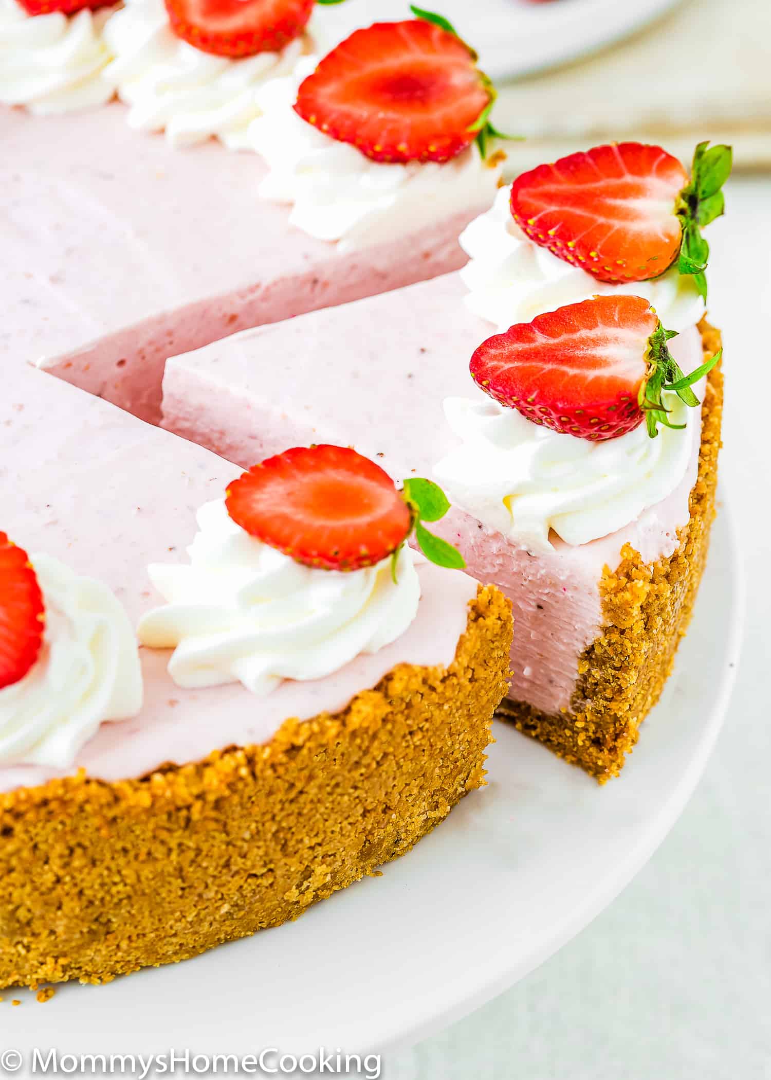 a sliced No-Bake Strawberry Cheesecake with fresh strawberries and whipped cream on top.