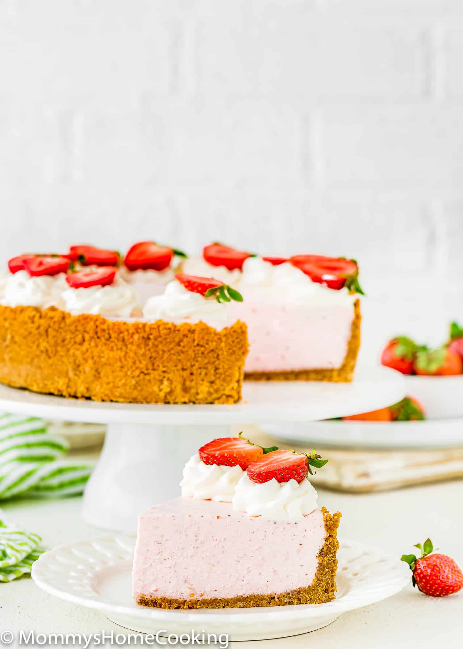 a slice of No-Bake Strawberry Cheesecake on a plate and the whole cake on the background.