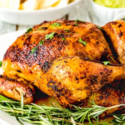 Venezuelan style roasted chicken over a plate with fresh rosemary.